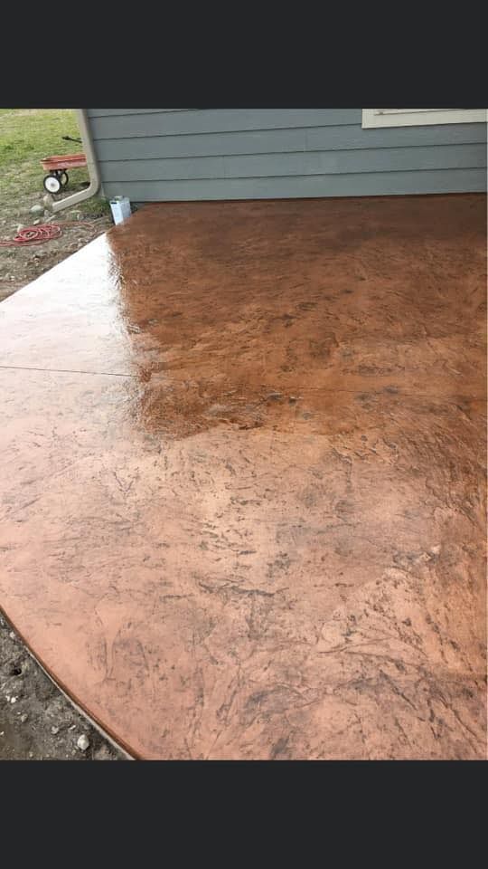 Brown stained concrete porch beside gray house siding and white railing.