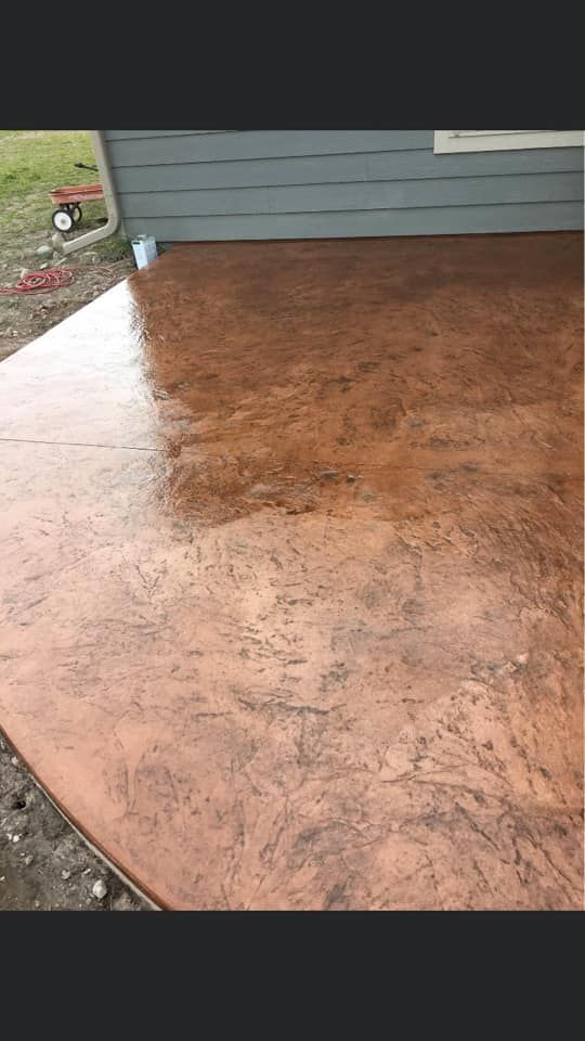 Rust-colored stamped concrete patio beside a gray house wall and open doorway