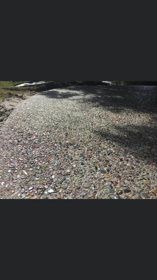 Gravel path bordered by grass and trees, with sunlight and shadows across the ground
