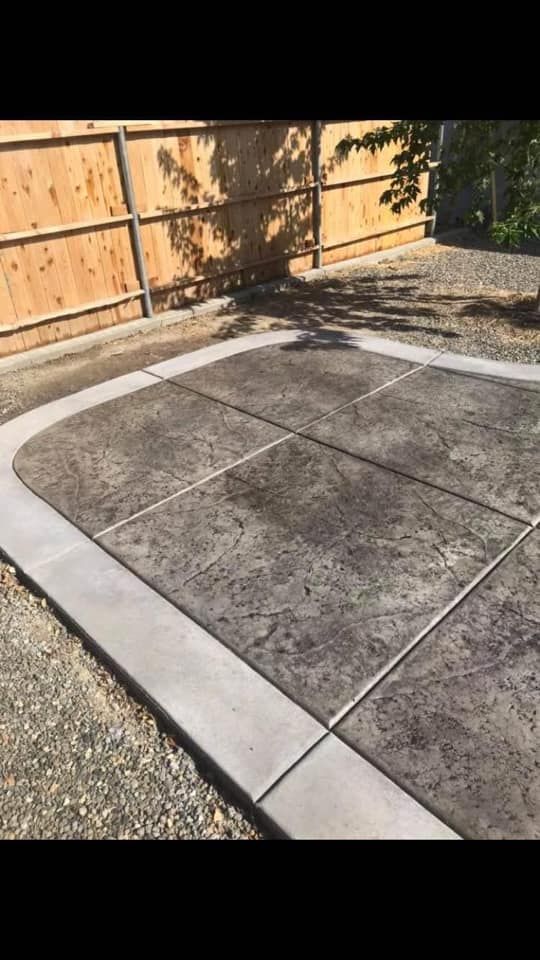 Empty concrete patio corner with gravel border and wooden fence in the background