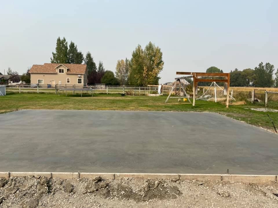Empty concrete court beside a grassy yard, with a house and small pavilion in the background.