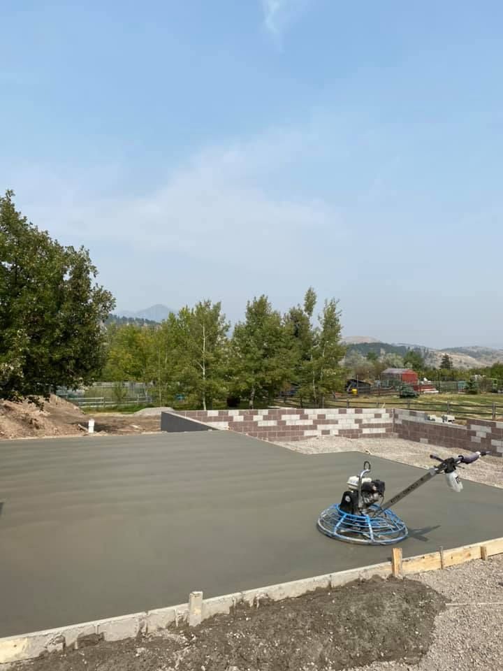 Concrete slab being finished with a power trowel in an outdoor construction site, with hills in the background