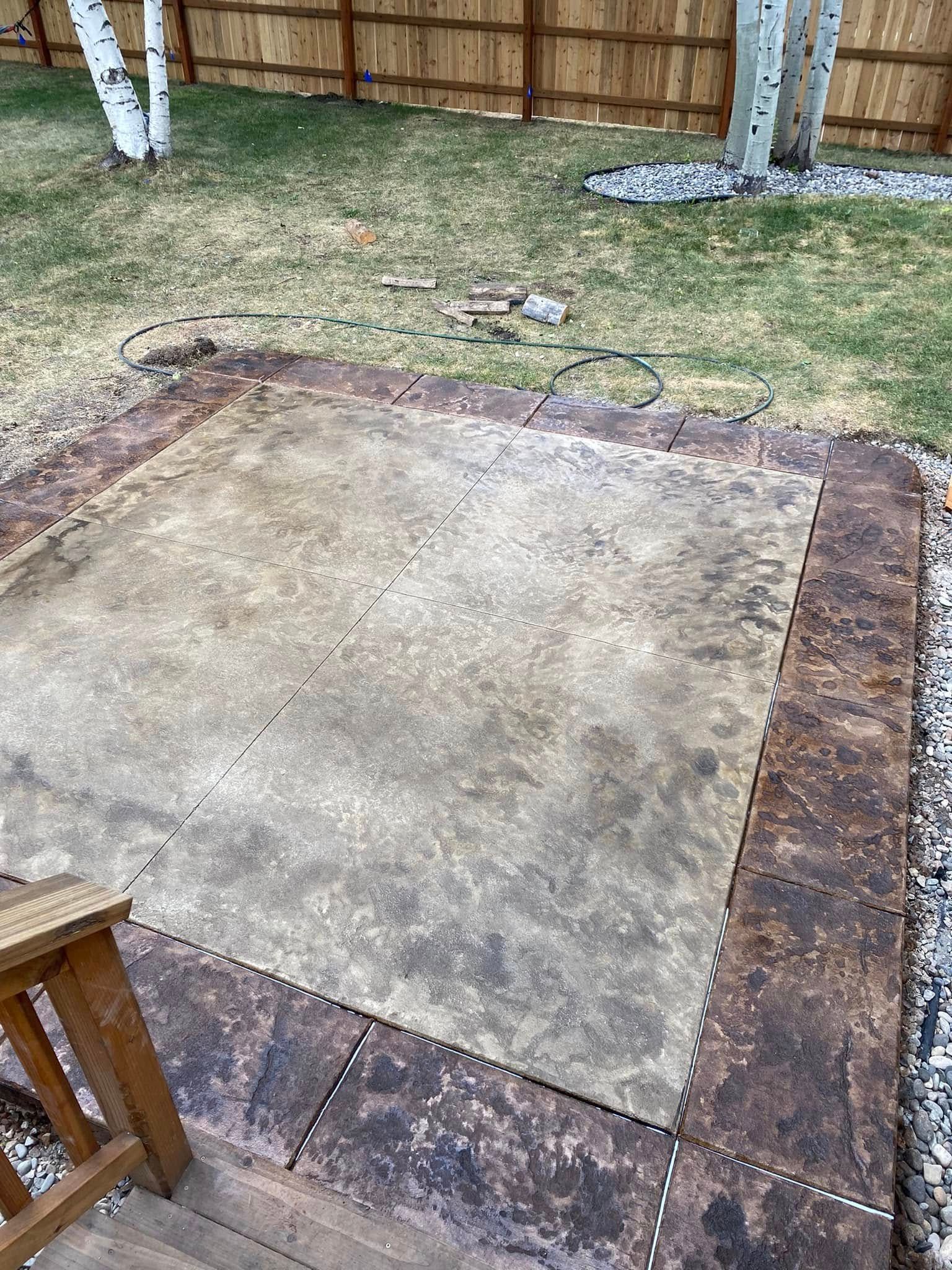 Concrete patio area in a fenced backyard with grass and two birch trees nearby