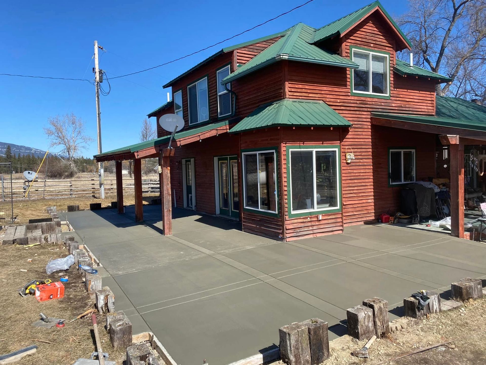 Red-sided house with green trim and a large concrete patio under construction on a sunny day