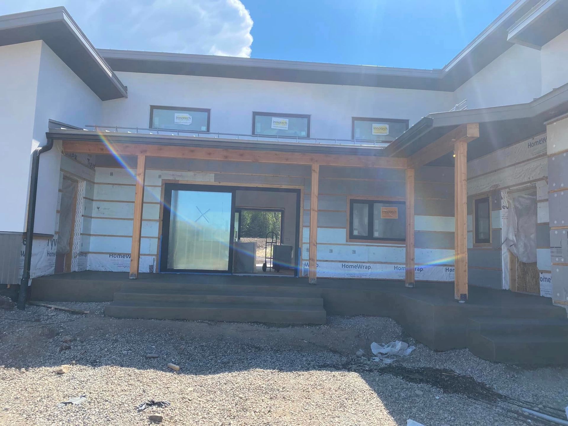 Modern two-story house exterior with covered front porch, stone siding, and gravel driveway under construction