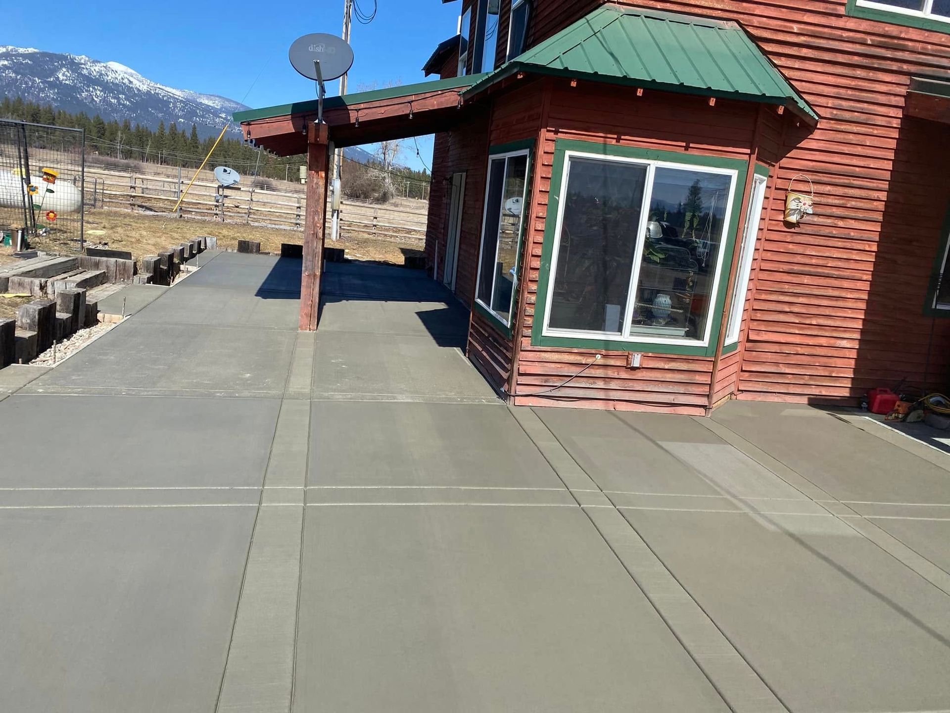 Sidewalk beside a red building with green roof, mountains in the background, and a satellite dish nearby