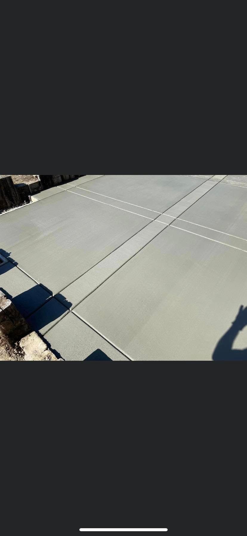 Sunlit concrete driveway with expansion joints and a shadow at the edge