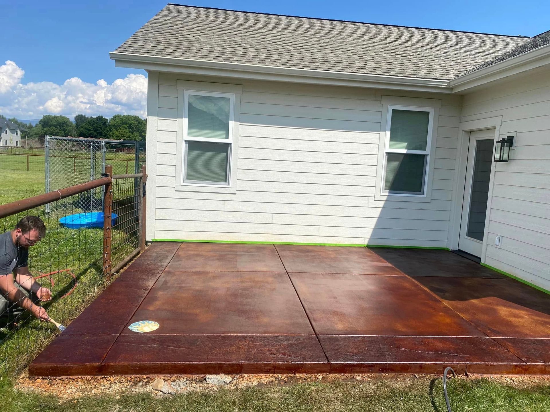 Rust-colored concrete patio beside a white house, with a person kneeling near the left edge.