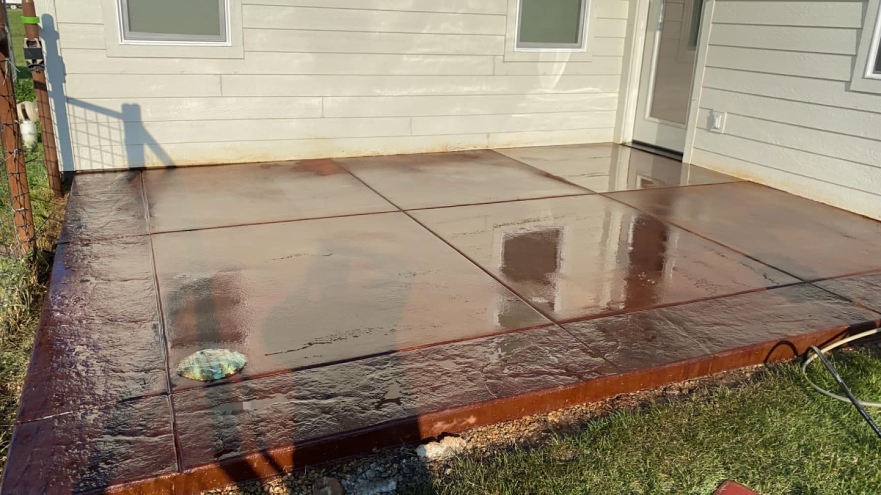 Wet concrete patio slab beside a house, reflecting sunlight near the back door