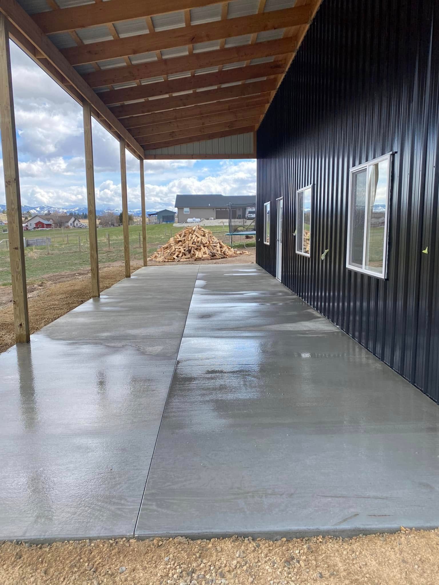Covered concrete walkway beside a black building, with a wooden roof and open field beyond.