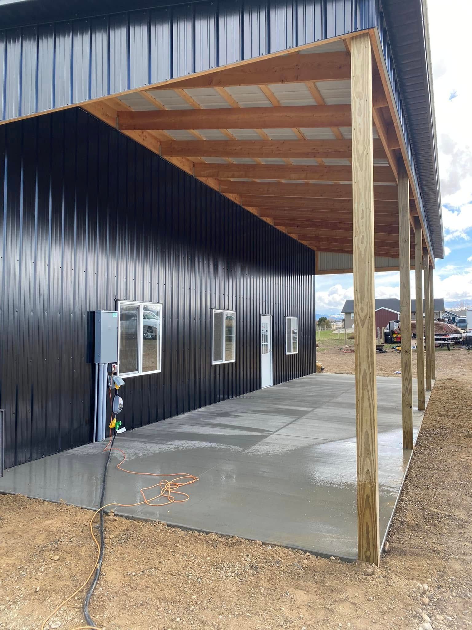 Black metal building with a concrete patio and covered wooden porch, seen from the side.