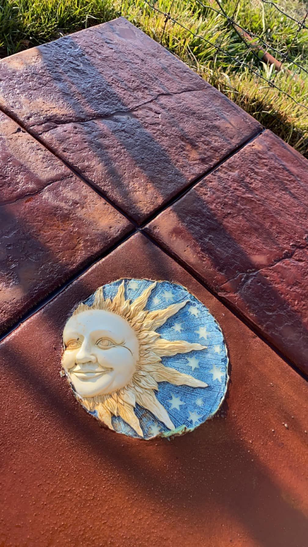 Small painted sun face ornament on a red wooden bench in sunlight.