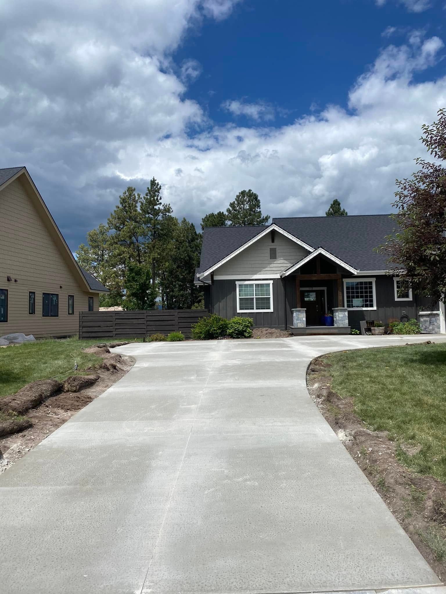 Concrete driveway leading to a gray house under a cloudy blue sky