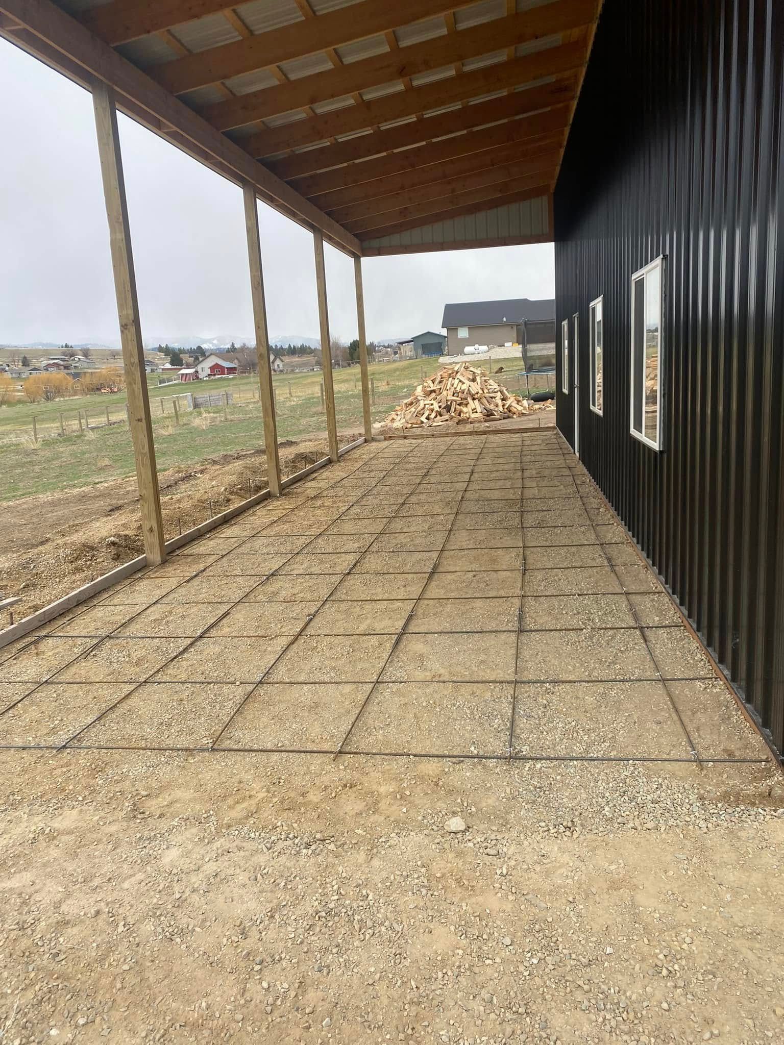 Covered porch beside a black building, with gravel ground, wooden posts, and a pile of rocks in a rural area