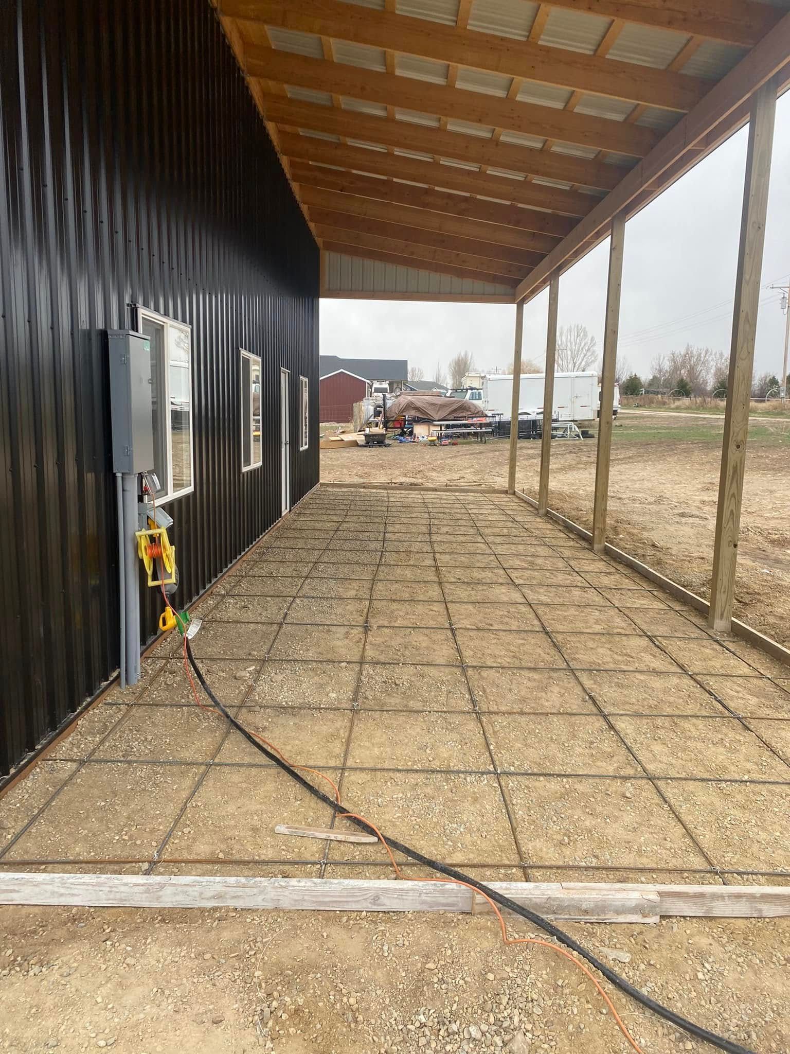 Covered gravel walkway beside a black metal building, with utility boxes and an open field beyond.