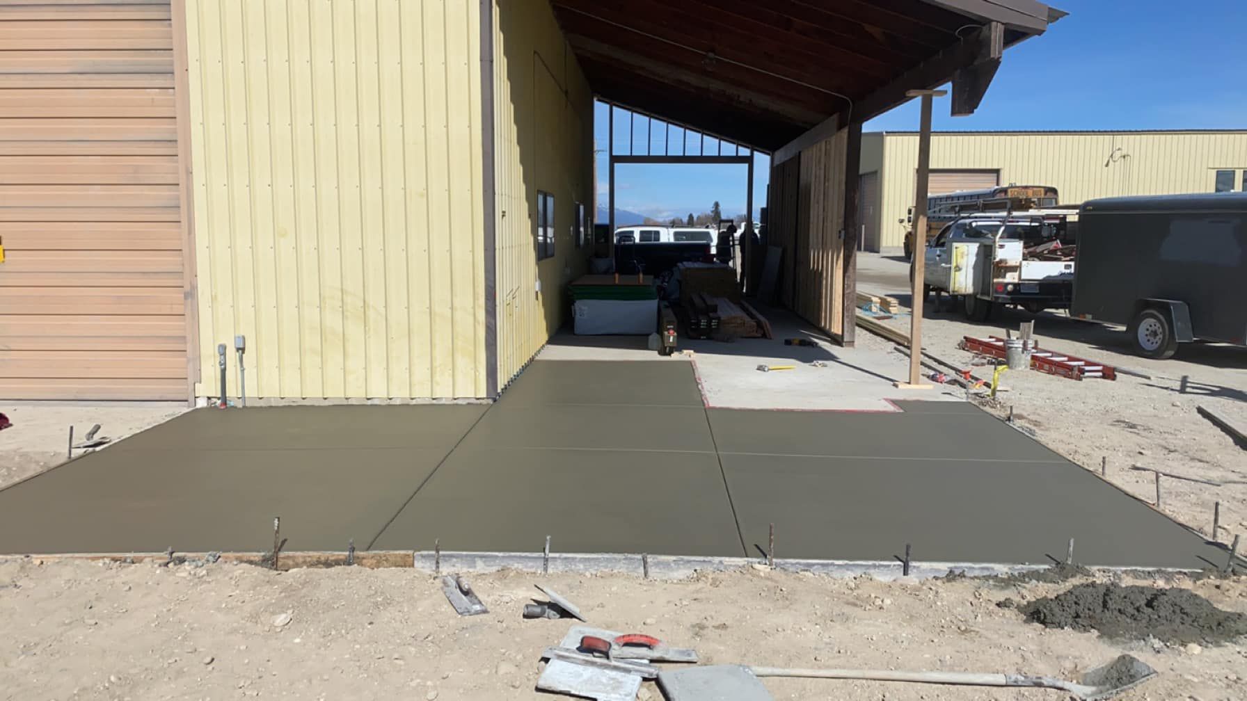 Outdoor concrete walkway and patio slabs beside a beige building with a covered porch and parked vehicles.
