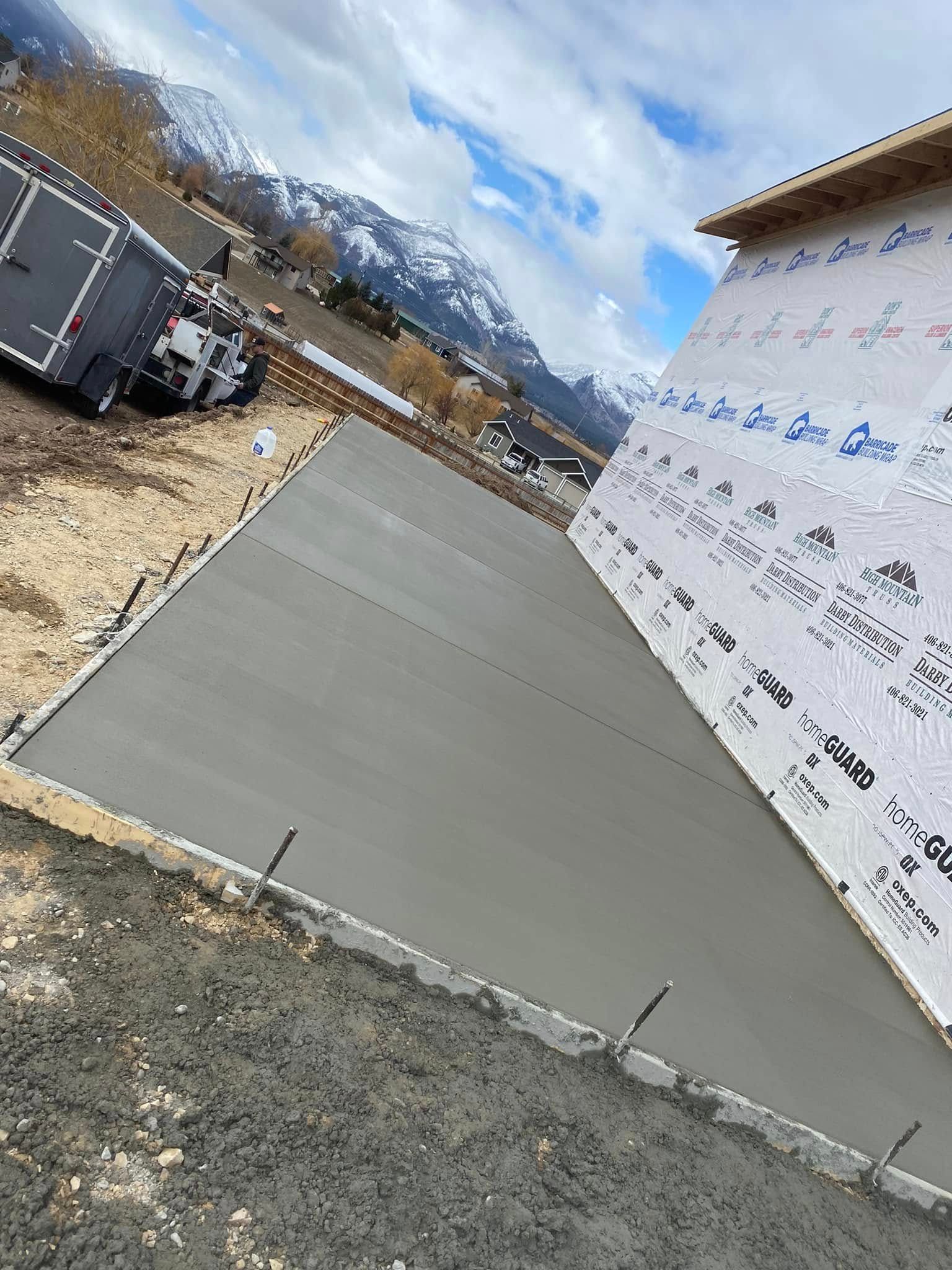 Fresh concrete driveway beside a house under construction, with mountains and parked vehicles in the background
