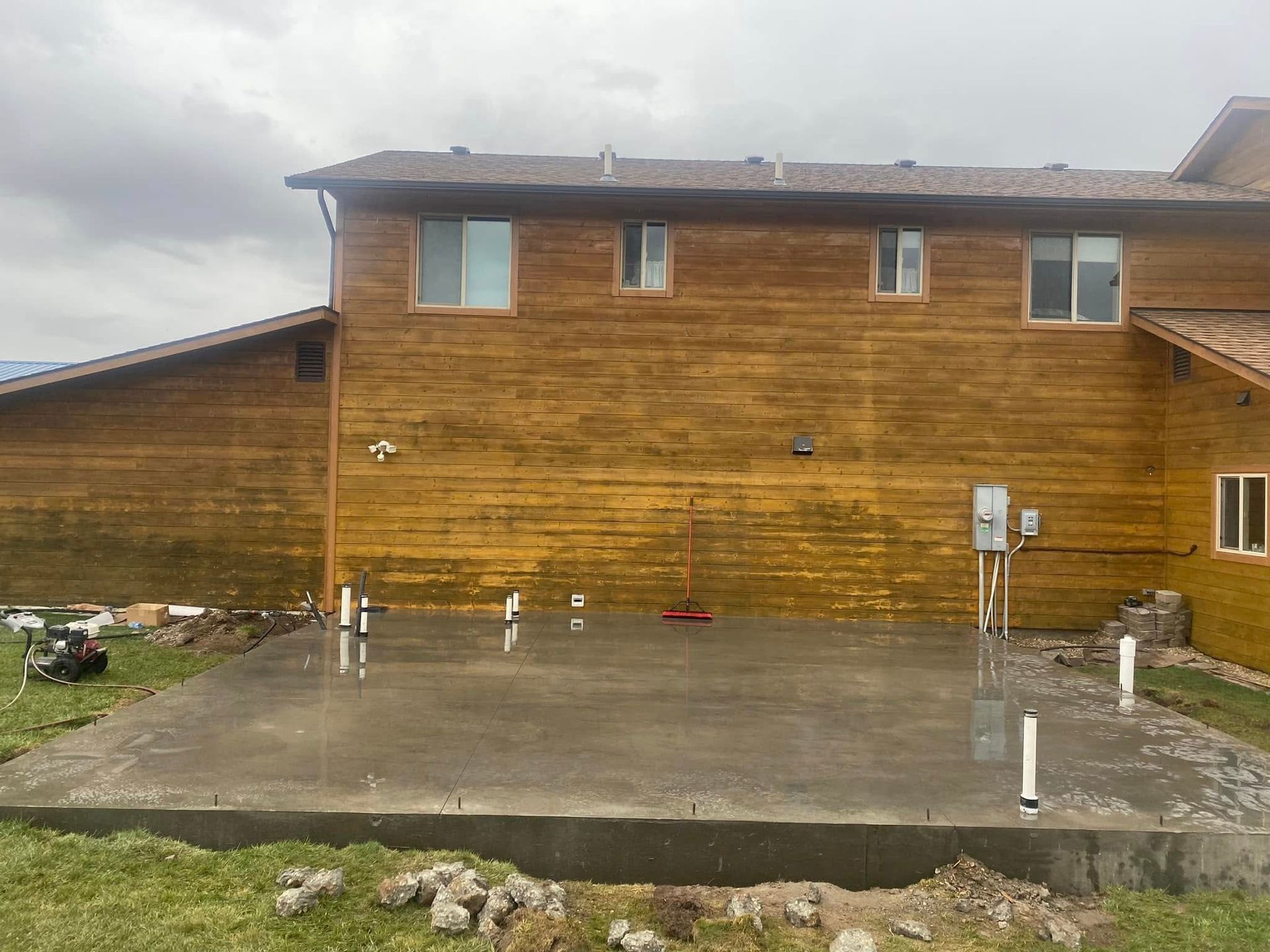 Wood-sided house with a wet concrete patio and cloudy sky after rain