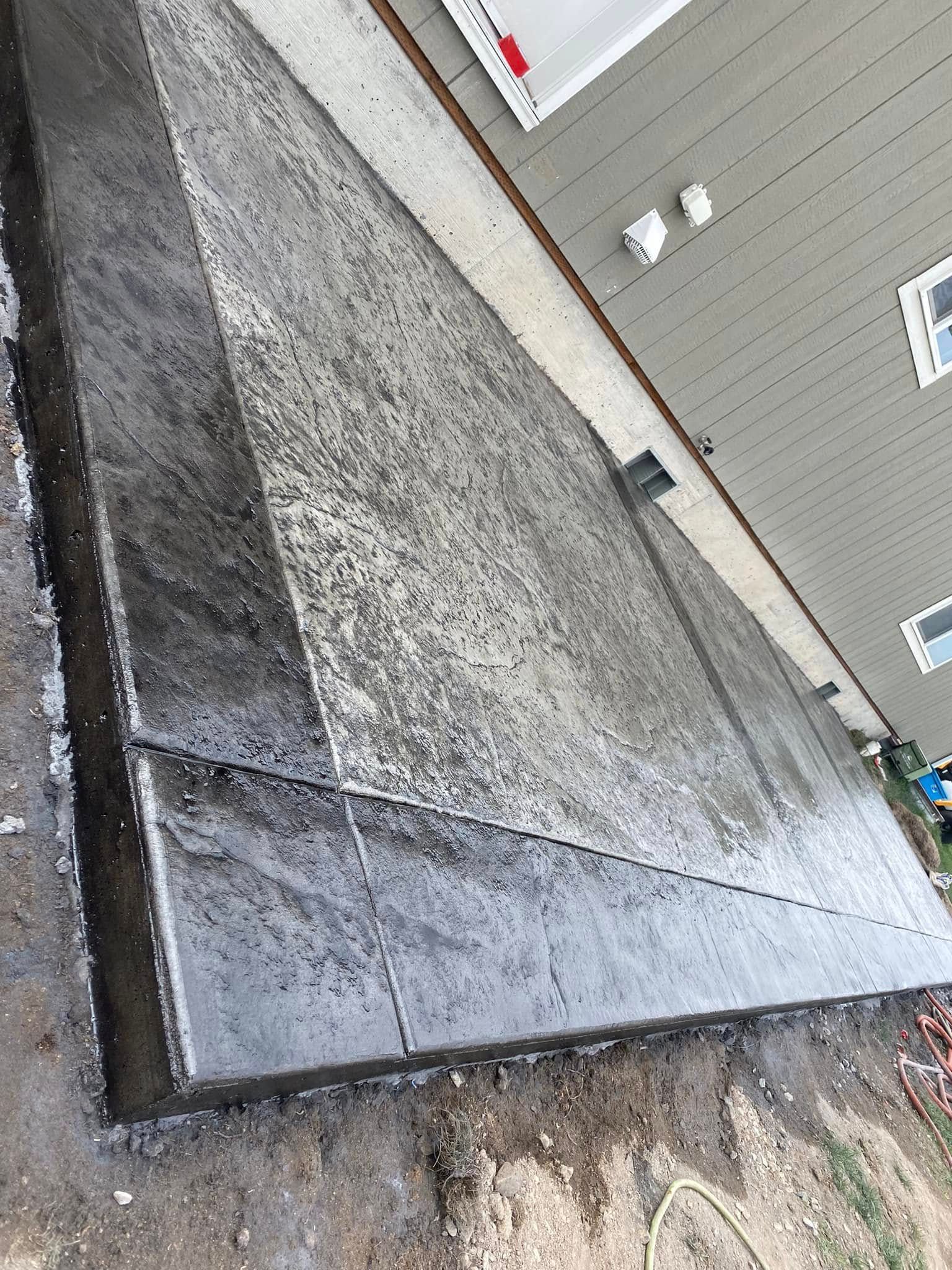 Sloped concrete retaining wall beside a building, with dark trim and gravel ground below.
