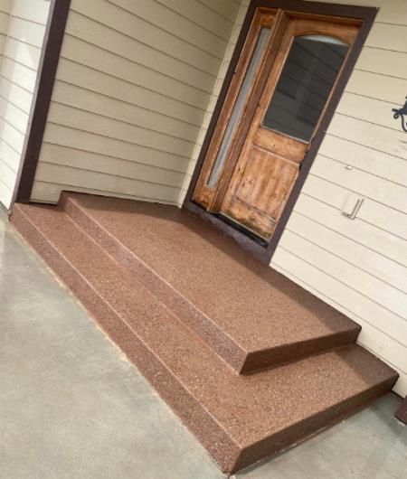 Small front porch with brown concrete steps and a wooden door on beige siding.