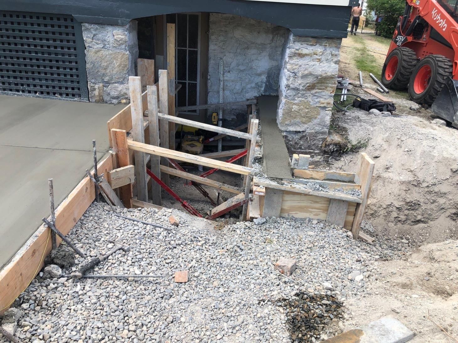 Foundation excavation beside a house with wooden shoring and construction equipment nearby
