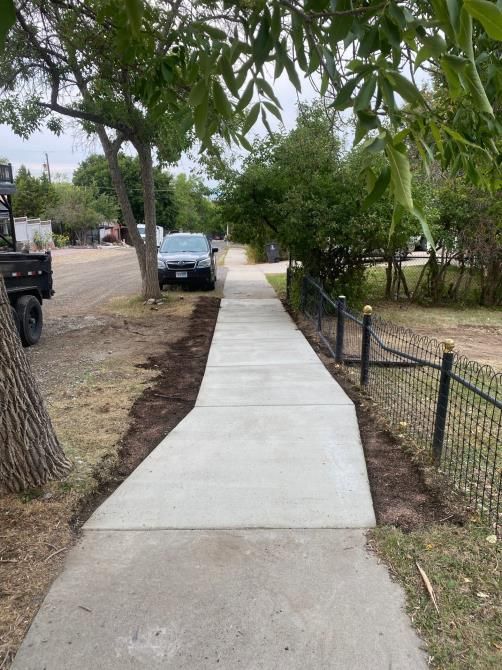 New concrete sidewalk along a residential street with a parked car and trees on both sides