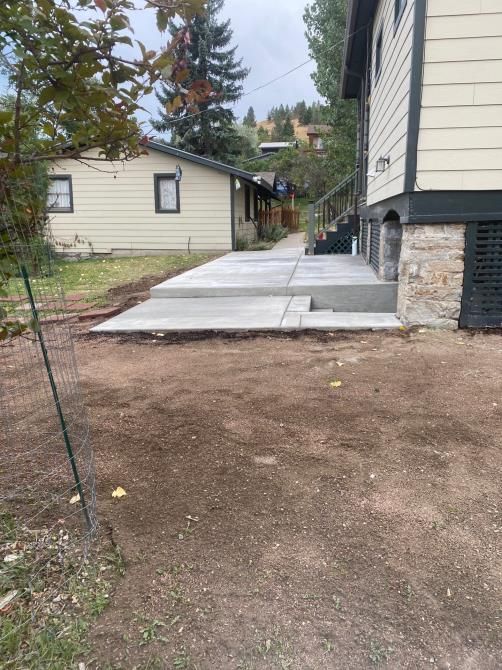 Concrete walkway beside a house with a gravel yard and a small shed in the background