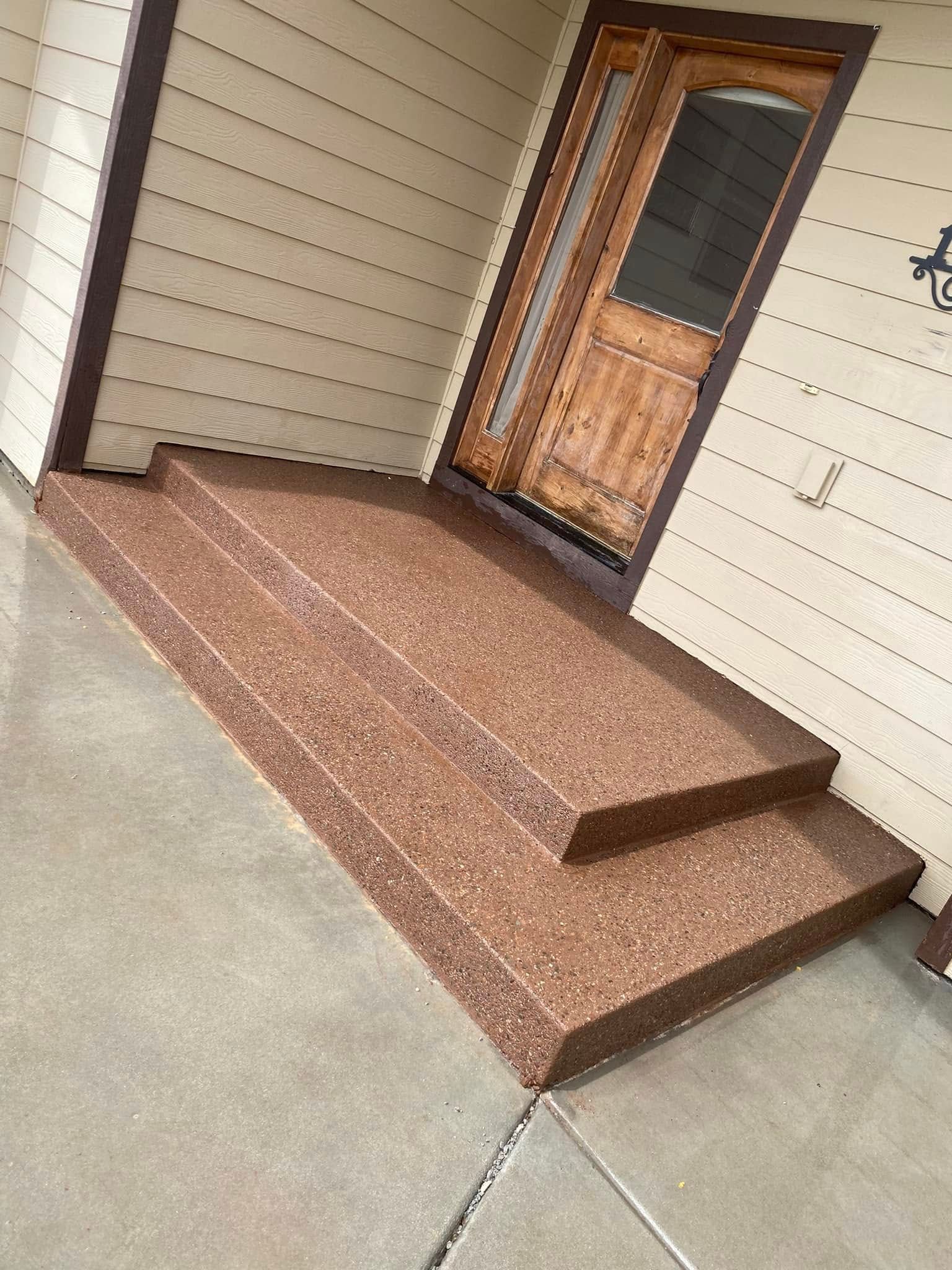 Front porch with tan siding, brown tiled steps, and a wooden front door.