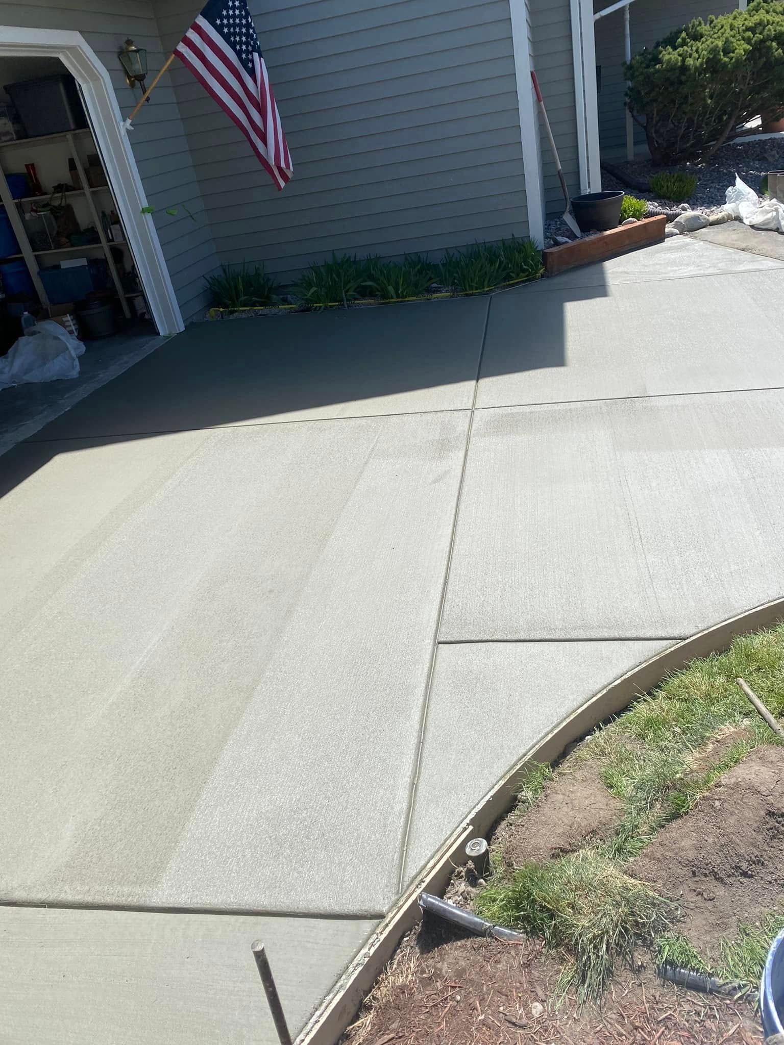 Concrete driveway and front walkway beside a house, with an American flag and small garden edge.
