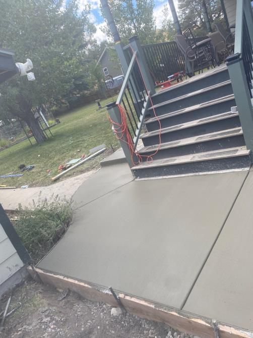 Concrete sidewalk ramp leading to a porch stairway with blue railings and a red handrail in a yard.
