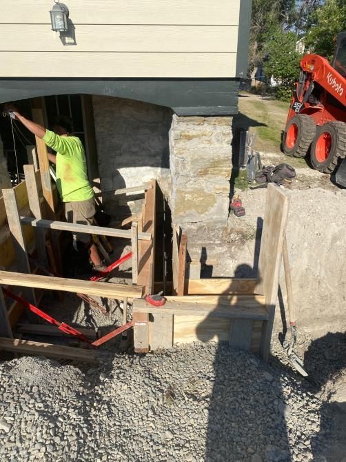 Worker building forms beside house foundation with gravel and an excavator nearby