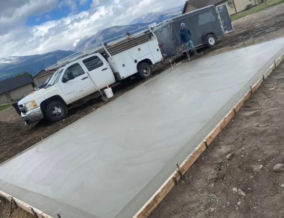 White utility truck with trailer beside a newly poured concrete slab at a construction site.