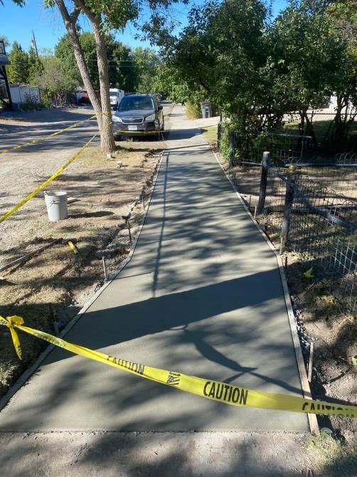 Blocked sidewalk under construction, with caution tape and trees along a suburban street.
