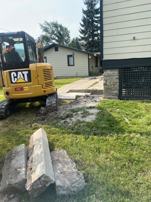 CAT excavator near a house foundation with concrete blocks and a grassy yard, under construction