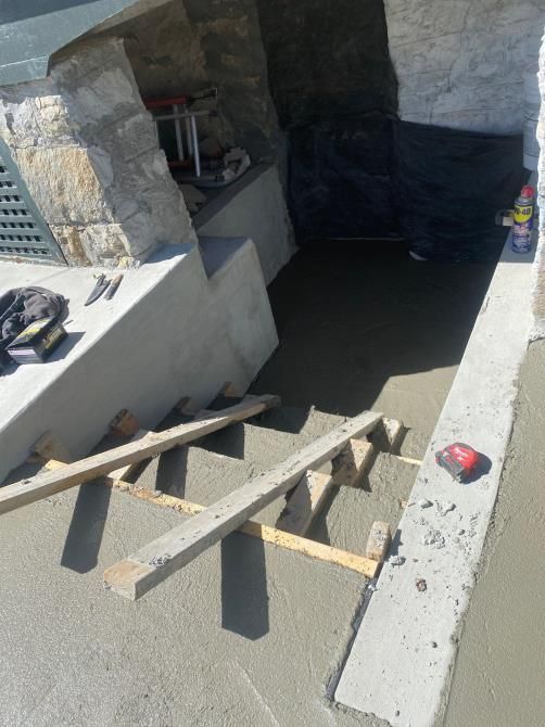 Temporary wooden stairs leading into a concrete stairwell under construction, with tools on a ledge.