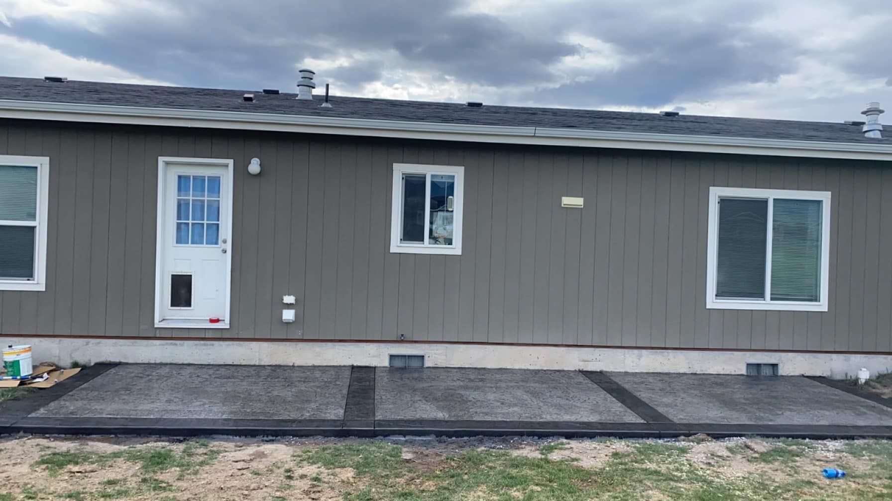 Gray house exterior with a white door, windows, and a concrete walkway under cloudy skies