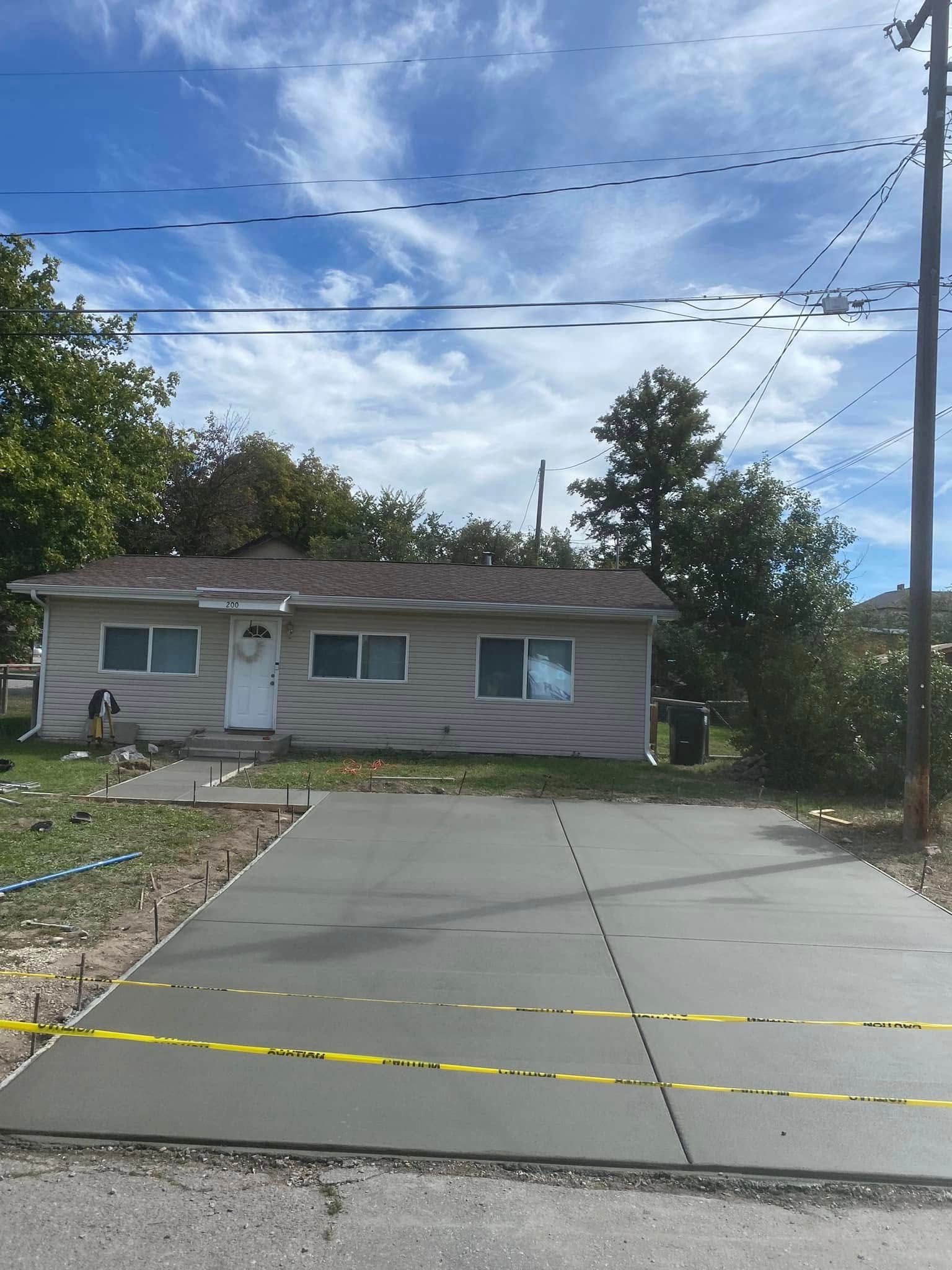 Single-story house with driveway, caution tape, and utility lines under a partly cloudy sky