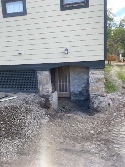 House with a damaged foundation and exposed basement entrance over rough dirt ground
