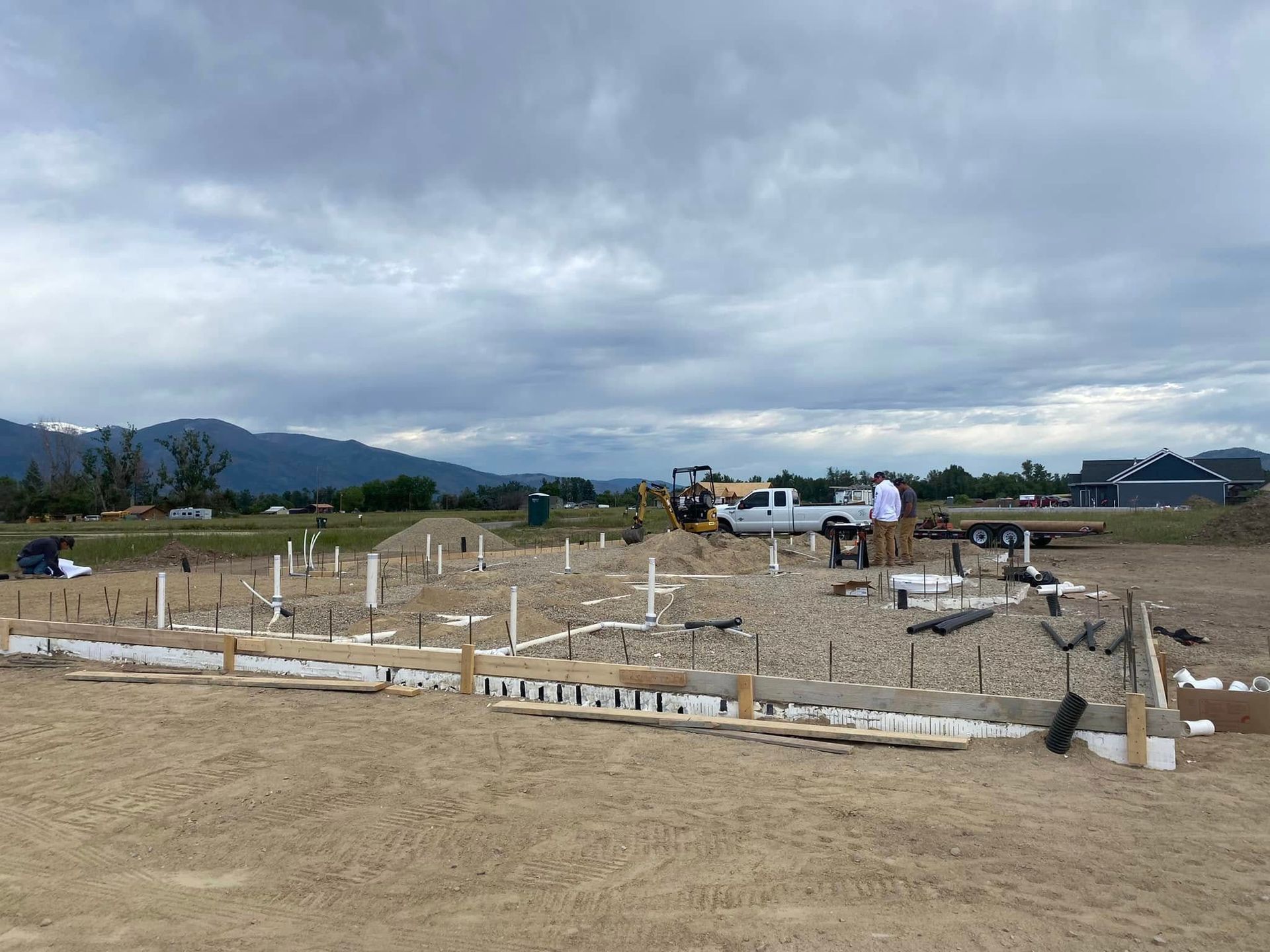 Construction site with a concrete foundation and wooden forms in an open field under cloudy skies
