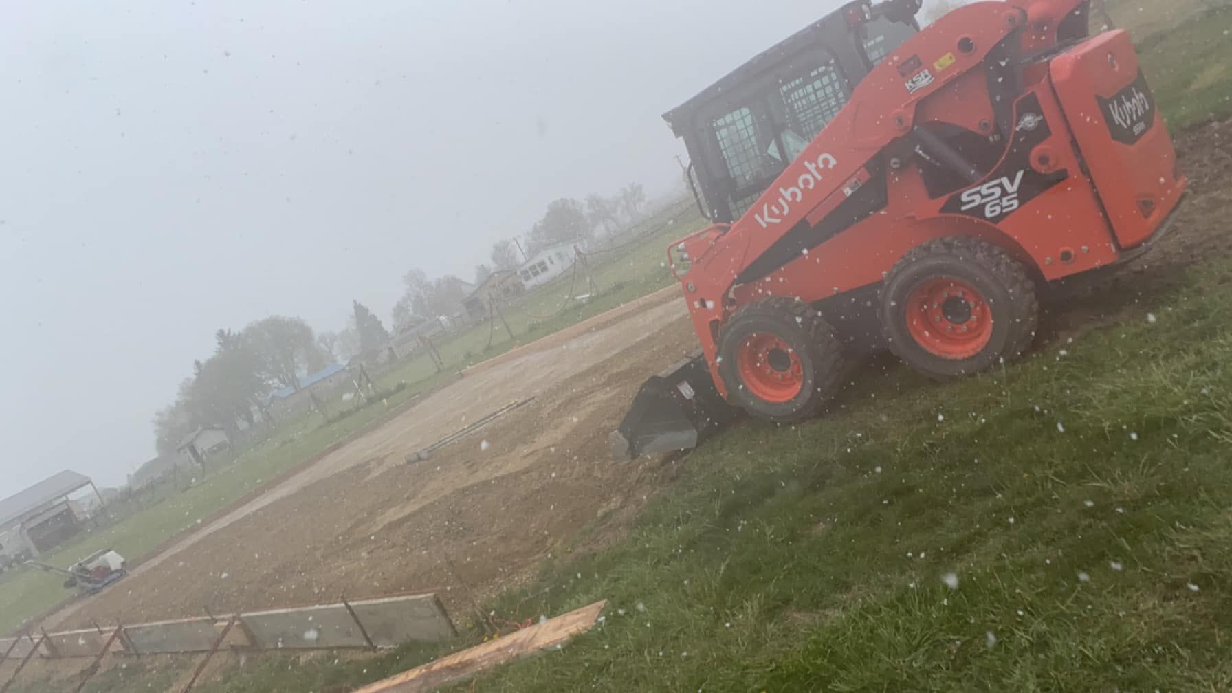 Red skid-steer loader on a muddy field in foggy weather