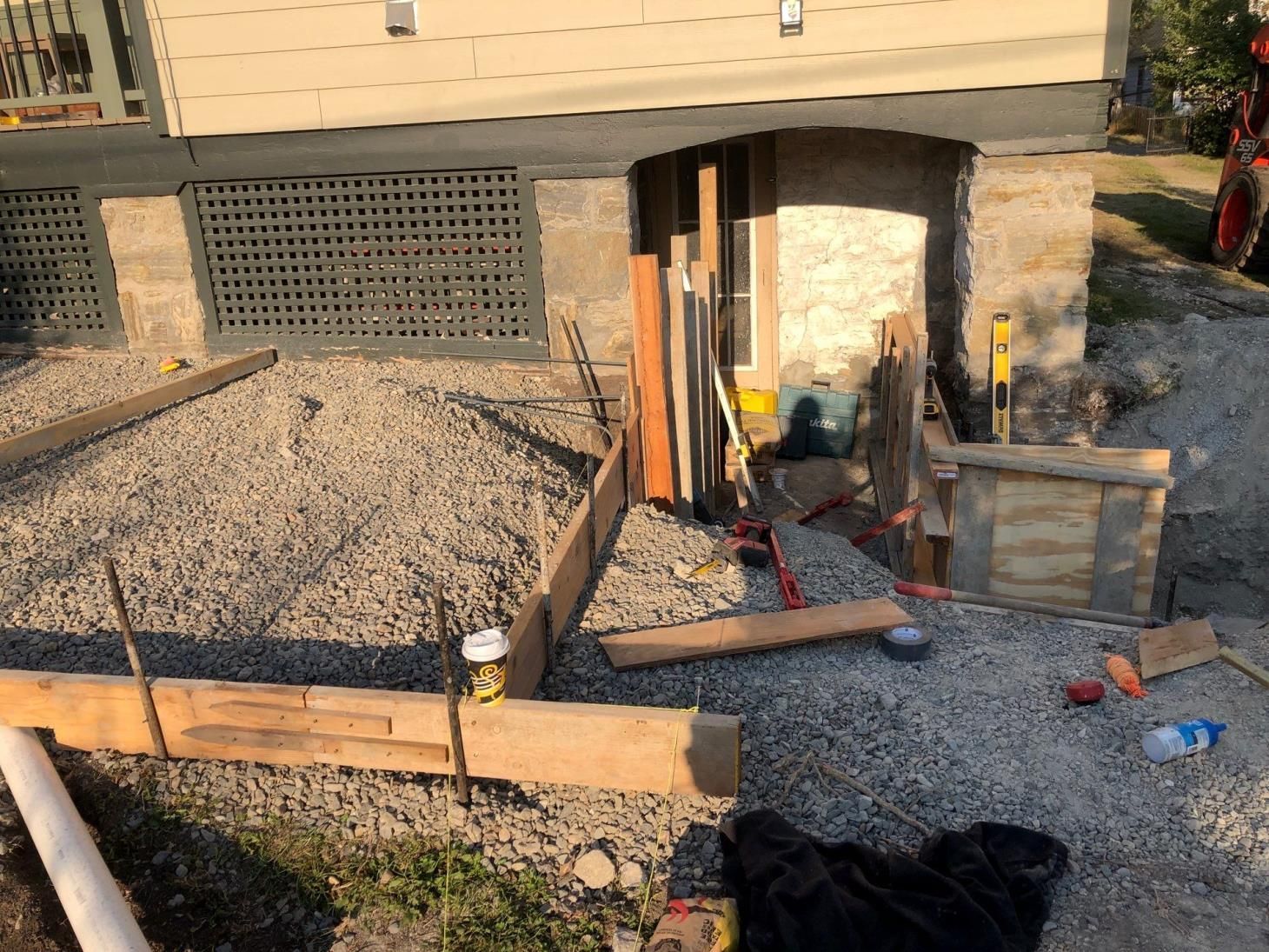 Backyard construction site with gravel, stone retaining wall, and tools near a basement entrance