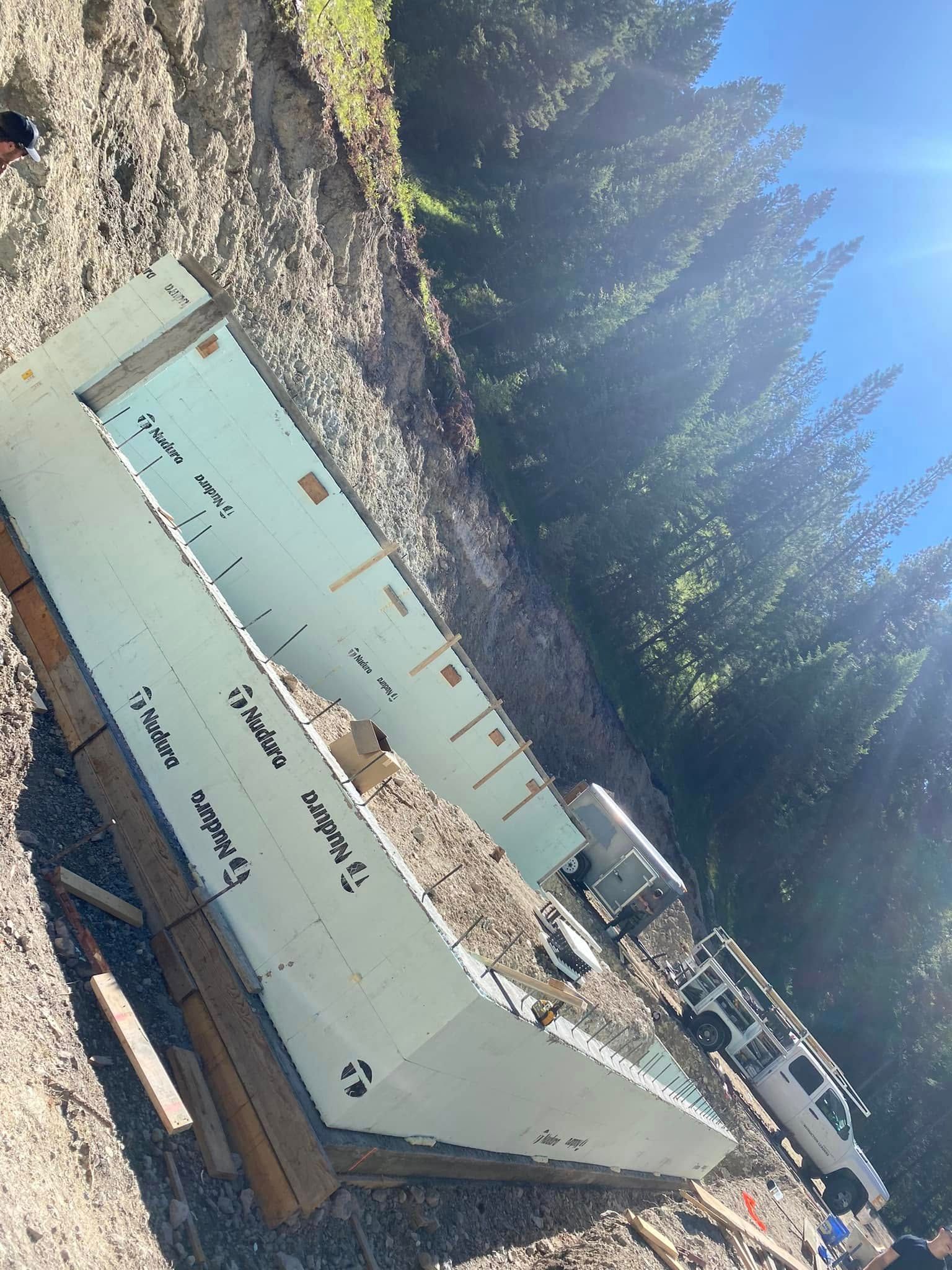 Overturned pale-green dumpster at a construction site beside a gravel road and trees