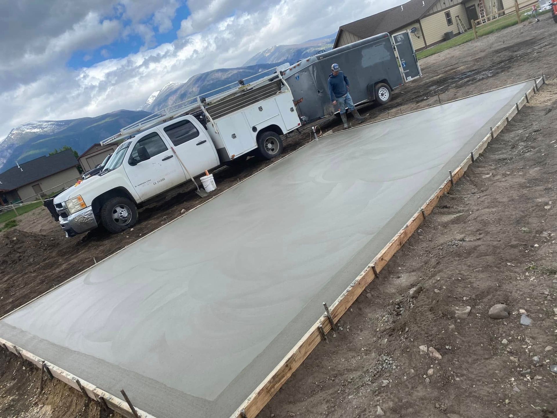 Freshly poured concrete slab beside a white truck and trailer at a construction site