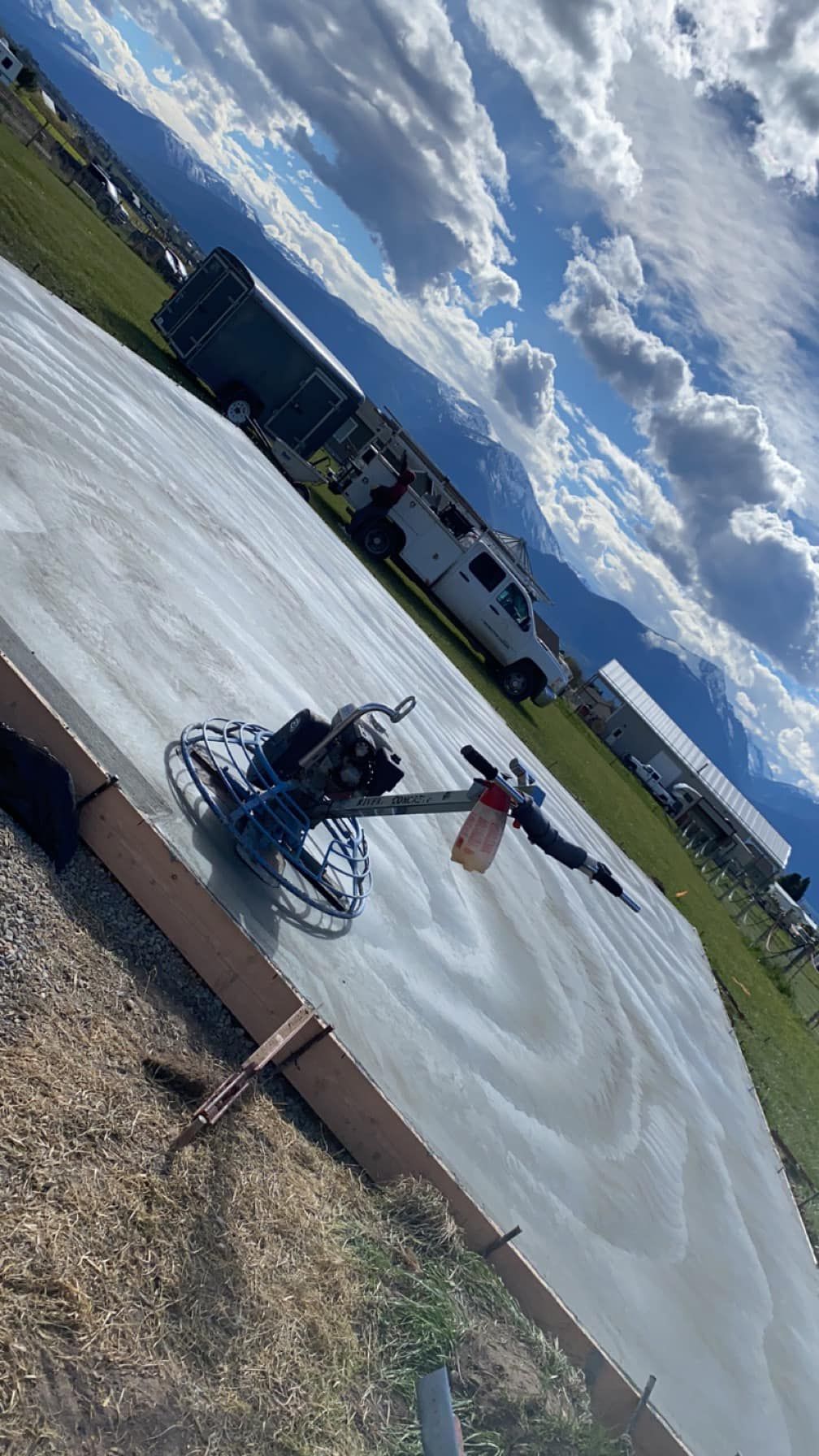 Person powerwashing a concrete pad outdoors near a truck under a cloudy sky