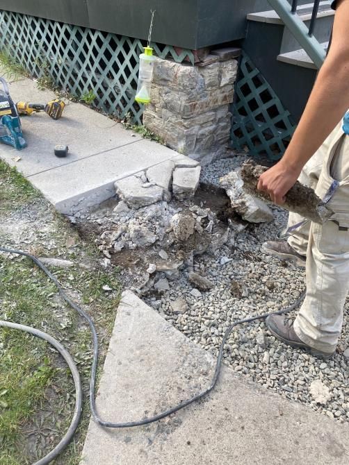 Damaged concrete steps with rubble and a person standing nearby beside a house exterior