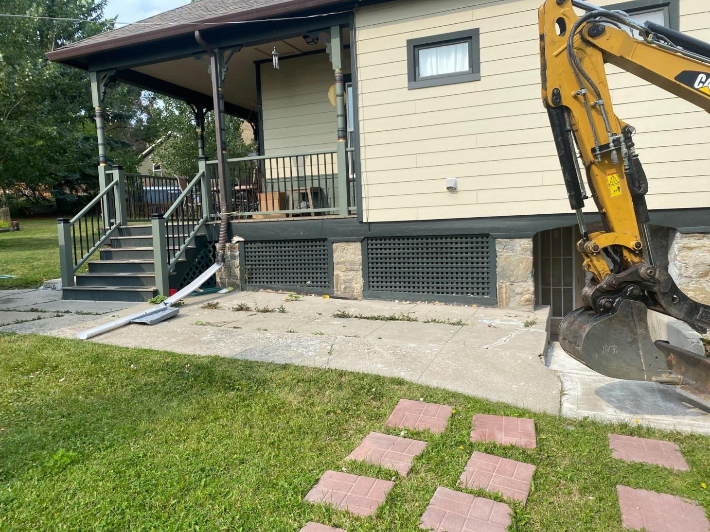 House exterior with front porch, steps, and an excavator digging beside a concrete path