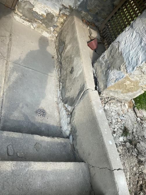 Cracked concrete steps beside a rough stone wall and narrow outdoor passage