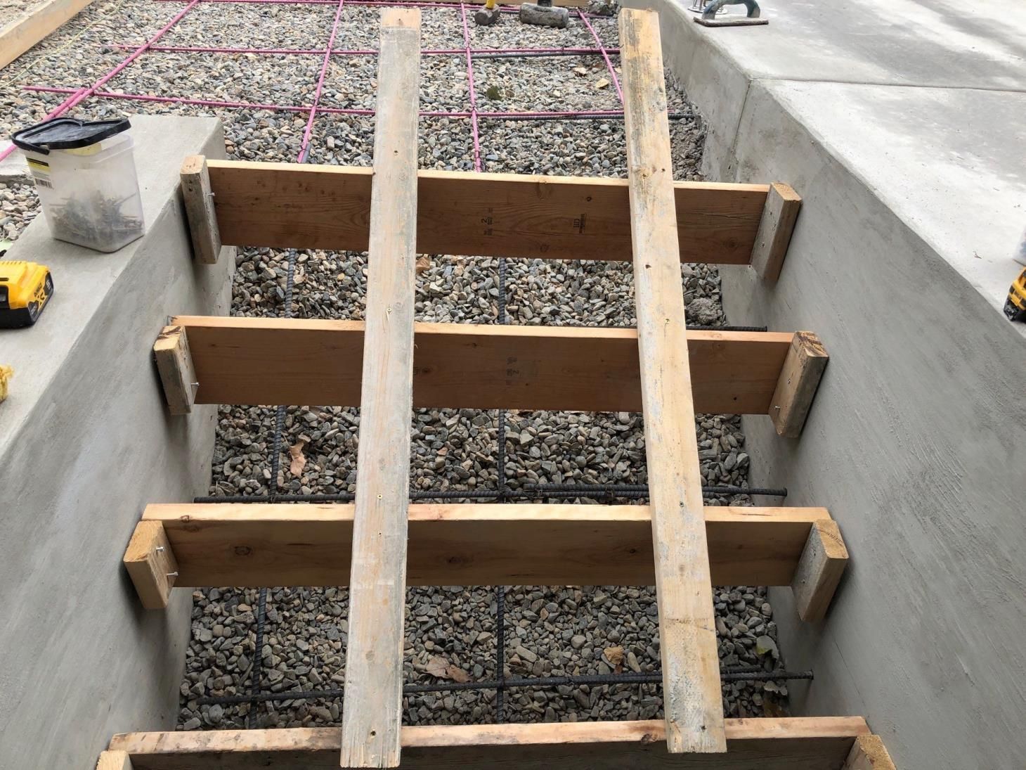 Wooden formwork beams spanning a gravel-filled trench in a concrete construction area