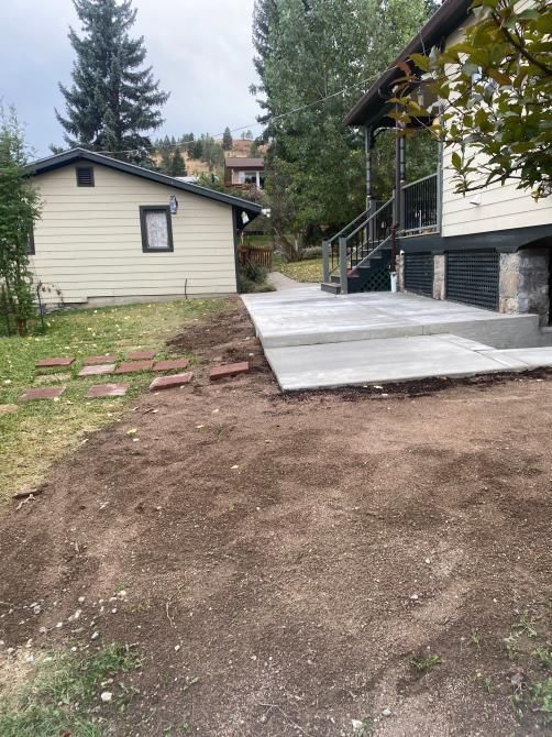 Backyard with a concrete patio beside a white house, dirt yard, and a small outbuilding.