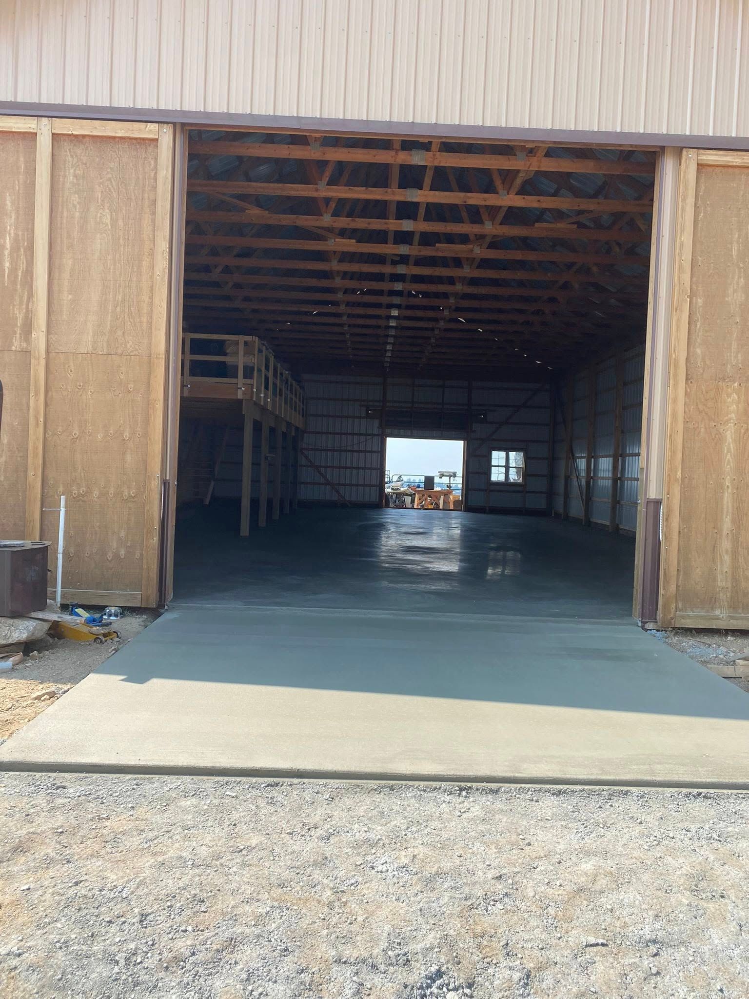 Open warehouse with large doors and a concrete floor, viewed from outside on gravel.